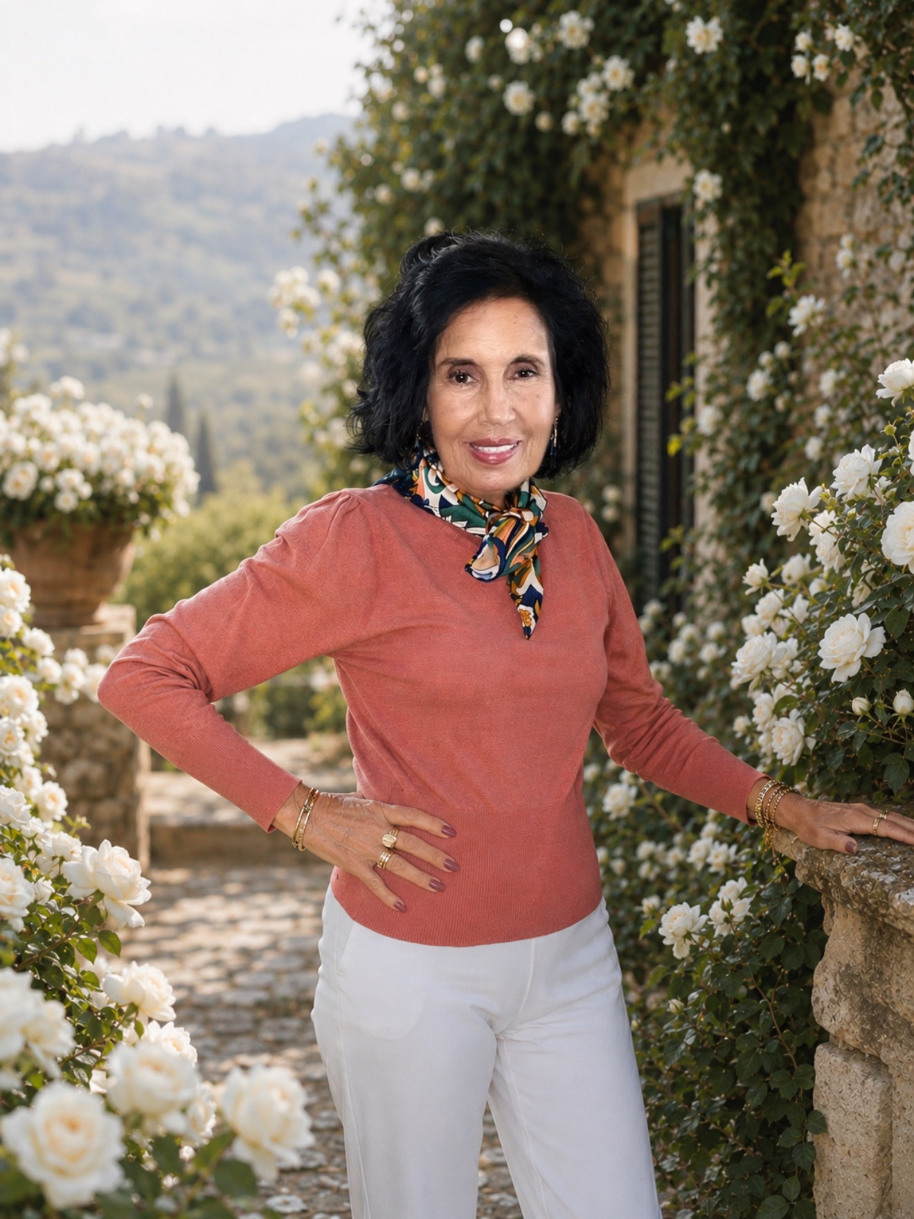 Elena Rosa Oddo standing among white roses in a sunlit garden